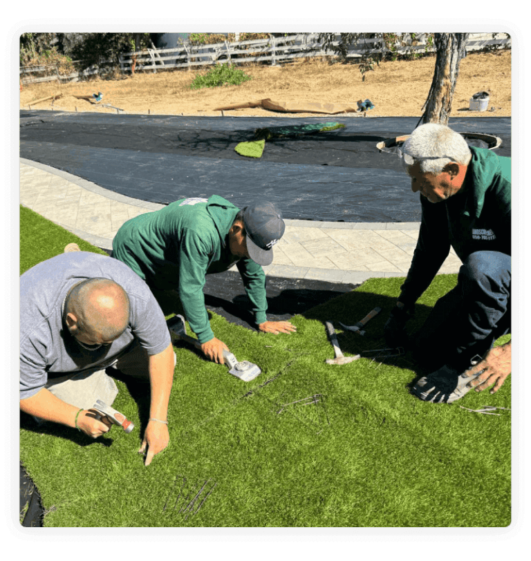 Three workers kneeling, installing artificial turf
